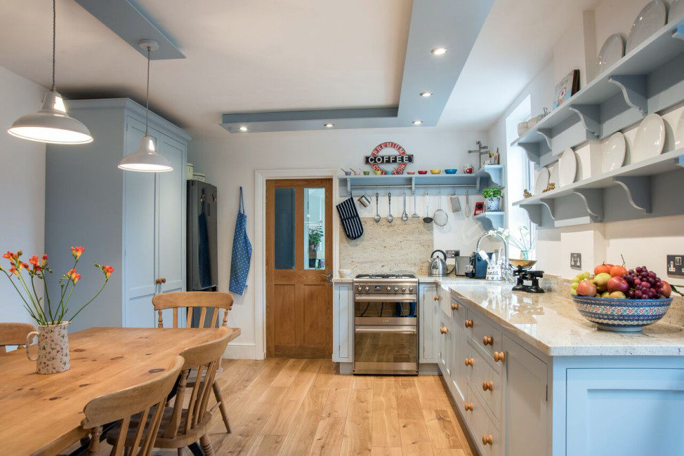 Inspiration for a large classic l-shaped kitchen/diner in Gloucestershire with a built-in sink, shaker cabinets, blue cabinets, granite worktops, brown splashback, stone slab splashback, stainless steel appliances, light hardwood flooring, no island and white worktops.