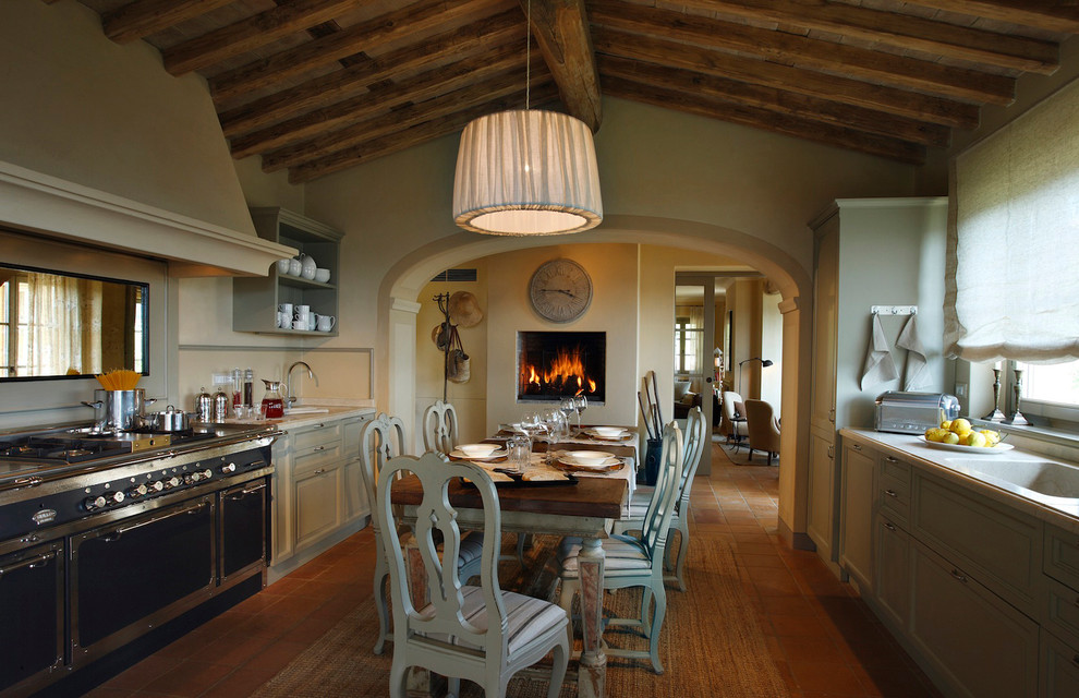 На фото: параллельная кухня в средиземноморском стиле с обеденным столом, фасадами с выступающей филенкой, серыми фасадами и черной техникой с