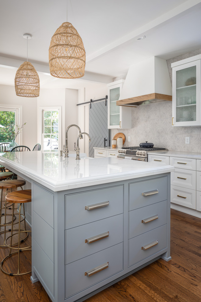 Mid-sized beach style u-shaped medium tone wood floor and brown floor open concept kitchen photo in Raleigh with a farmhouse sink, recessed-panel cabinets, white cabinets, quartzite countertops, multicolored backsplash, porcelain backsplash, stainless steel appliances, an island and white countertops
