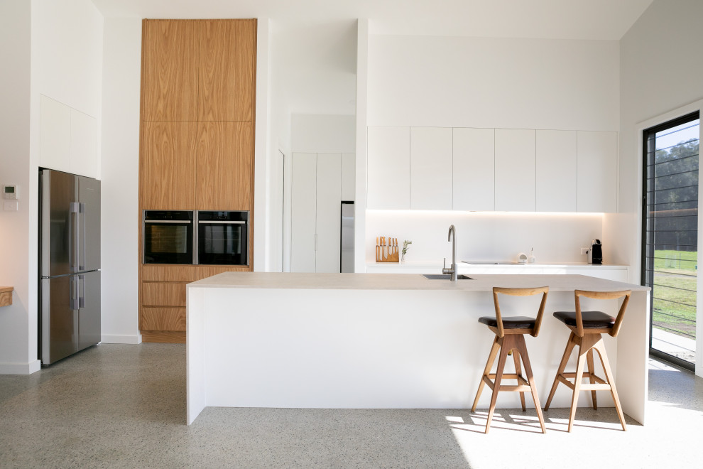 Idéer för att renovera ett stort funkis vit vitt kök, med släta luckor, vita skåp, bänkskiva i kvarts, vitt stänkskydd, betonggolv, en köksö, en enkel diskho, rostfria vitvaror och grått golv