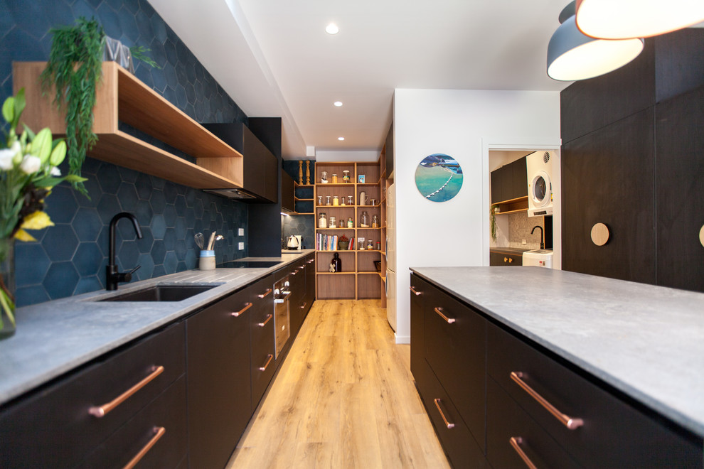 Ejemplo de cocina comedor contemporánea de tamaño medio con puertas de armario negras, encimera de acrílico, salpicadero azul, electrodomésticos de acero inoxidable, suelo de madera clara y una isla