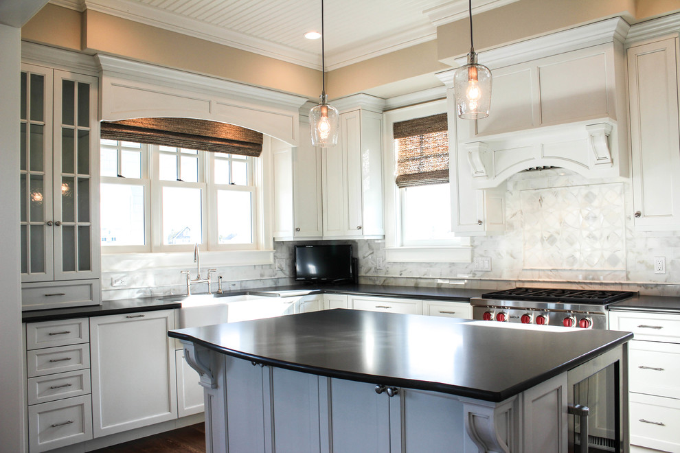 Example of a large beach style u-shaped medium tone wood floor open concept kitchen design in New York with a farmhouse sink, beaded inset cabinets, white cabinets, marble countertops, white backsplash, porcelain backsplash, black appliances and an island