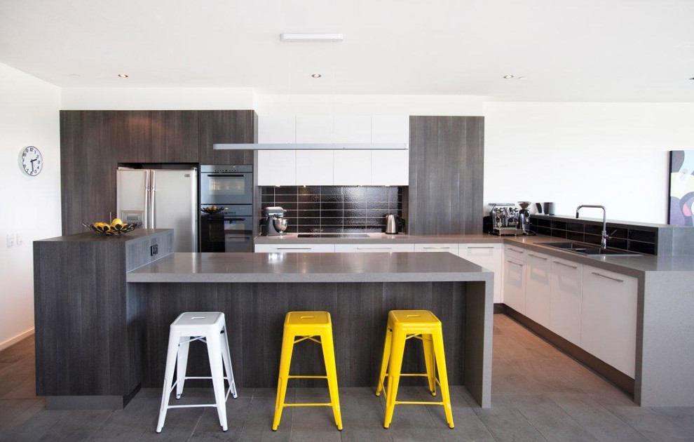 Expansive contemporary l-shaped kitchen/diner in Melbourne with a double-bowl sink, flat-panel cabinets, white cabinets, composite countertops, black splashback, ceramic splashback, black appliances, an island and ceramic flooring.