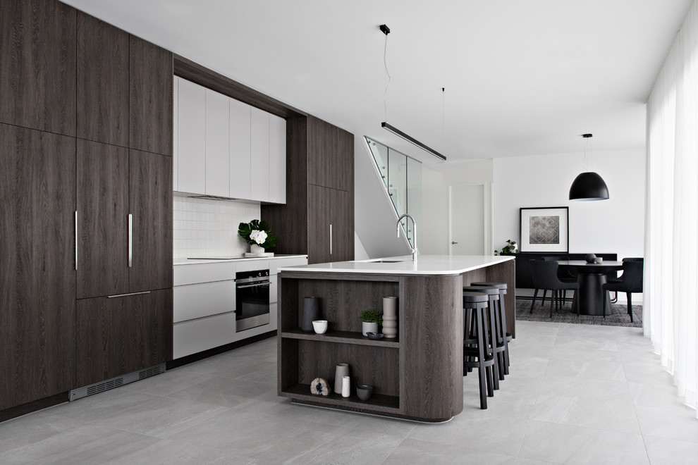 Exemple d'une cuisine parallèle tendance avec un évier encastré, un placard à porte plane, des portes de placard grises, un électroménager en acier inoxydable, îlot, un sol gris et un plan de travail blanc.