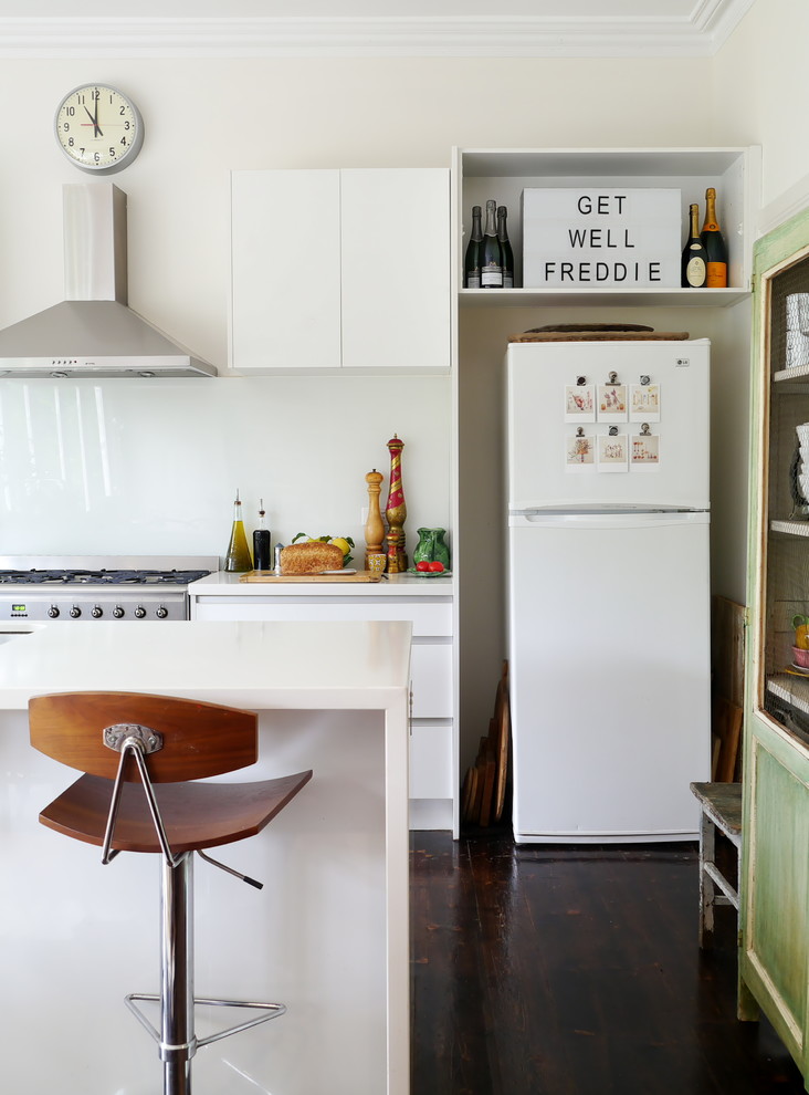 Stilmix Küche mit weißen Elektrogeräten, flächenbündigen Schrankfronten, weißen Schränken, dunklem Holzboden und Kücheninsel in Melbourne