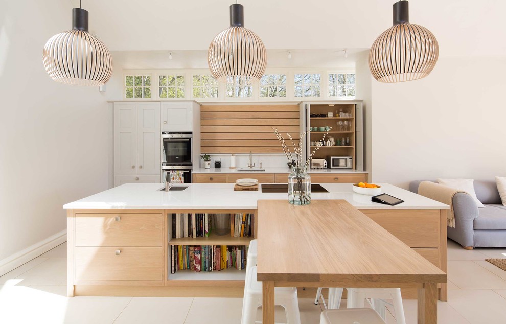 Cette image montre une cuisine ouverte parallèle design en bois clair avec un évier encastré, un placard à porte plane, un électroménager en acier inoxydable et îlot.