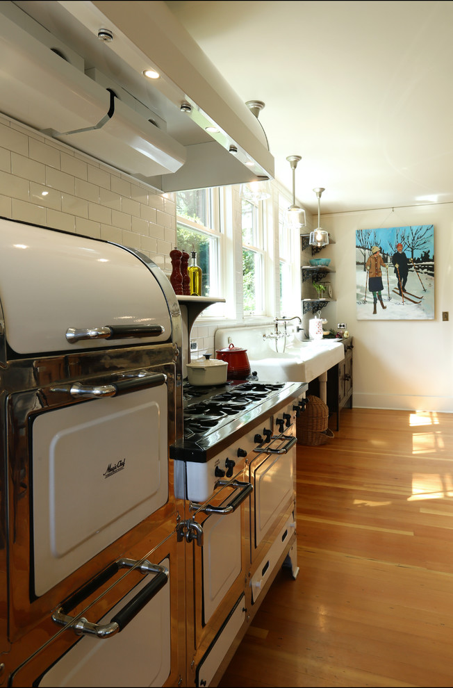 Example of a medium tone wood floor kitchen design in Portland with a farmhouse sink, white backsplash, ceramic backsplash, white appliances and an island