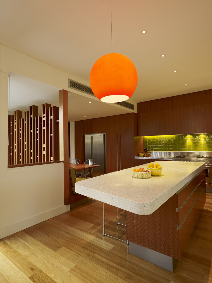 Mid-sized trendy l-shaped medium tone wood floor eat-in kitchen photo in Sydney with stainless steel appliances, flat-panel cabinets, dark wood cabinets, green backsplash, ceramic backsplash, granite countertops and an island