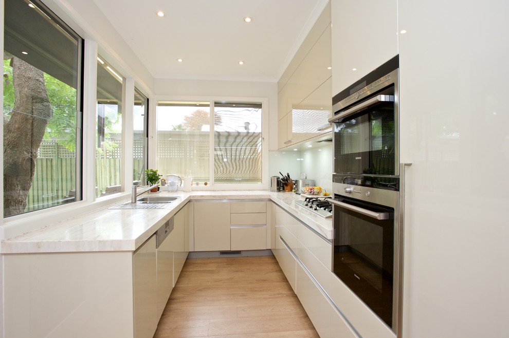 This is an example of a small contemporary u-shaped kitchen in Other with glass sheet splashback, stainless steel appliances and no island.