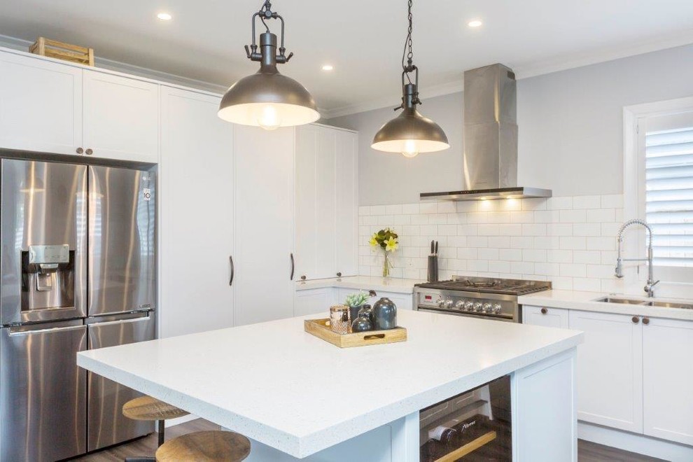 Photo of an expansive rustic u-shaped open plan kitchen in Wellington with white cabinets, engineered stone countertops, white splashback, ceramic splashback, laminate floors, an island, grey floors, white worktops, a built-in sink, recessed-panel cabinets and stainless steel appliances.