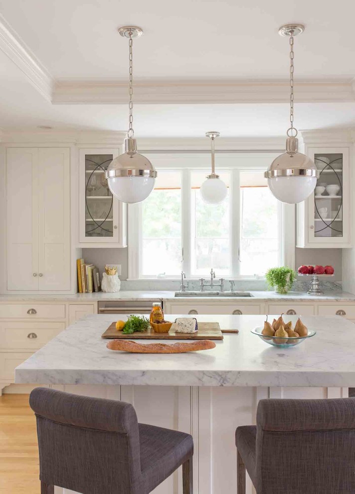 Example of a mid-sized classic light wood floor eat-in kitchen design in Boston with an undermount sink, shaker cabinets, white cabinets, marble countertops, white backsplash, subway tile backsplash, stainless steel appliances and an island