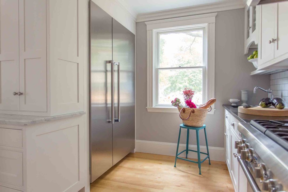 Eat-in kitchen - mid-sized traditional light wood floor eat-in kitchen idea in Boston with an undermount sink, shaker cabinets, white cabinets, marble countertops, white backsplash, subway tile backsplash, stainless steel appliances and an island