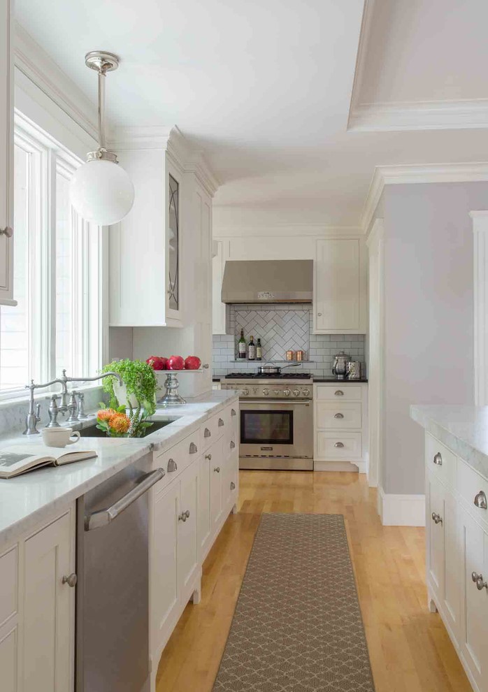 Klassisk inredning av ett mellanstort kök och matrum, med en undermonterad diskho, skåp i shakerstil, vita skåp, marmorbänkskiva, stänkskydd i tunnelbanekakel, rostfria vitvaror, ljust trägolv, en köksö och vitt stänkskydd
