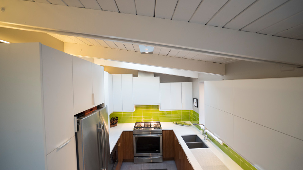 Idéer för att renovera ett mellanstort funkis vit vitt kök, med en undermonterad diskho, släta luckor, vita skåp, bänkskiva i kvarts, grönt stänkskydd, stänkskydd i glaskakel, vita vitvaror, klinkergolv i porslin och beiget golv