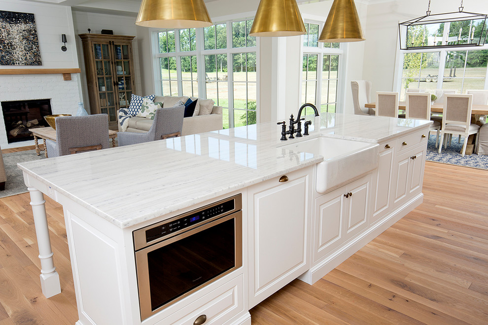 This is an example of a large rural l-shaped kitchen/diner in Columbus with a belfast sink, raised-panel cabinets, white cabinets, marble worktops, white splashback, mosaic tiled splashback, stainless steel appliances, light hardwood flooring and an island.