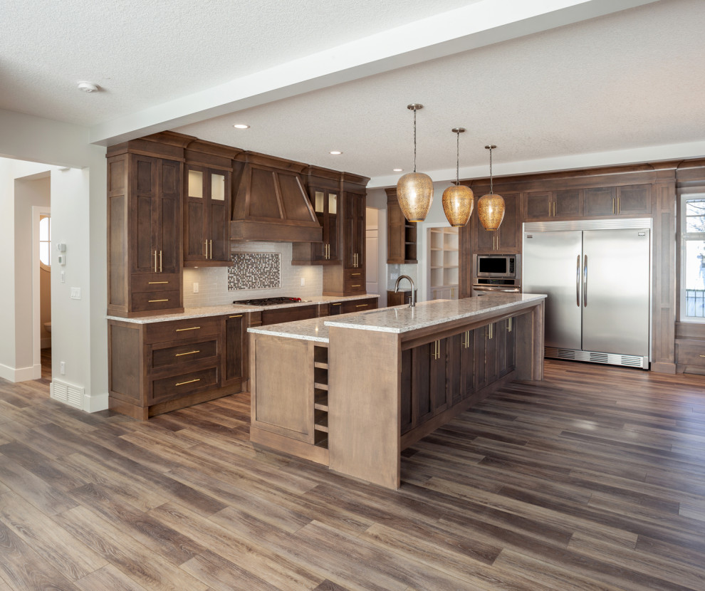 Photo of a medium sized classic l-shaped kitchen/diner in Calgary with a submerged sink, recessed-panel cabinets, dark wood cabinets, marble worktops, multi-coloured splashback, ceramic splashback, stainless steel appliances, dark hardwood flooring, an island, brown floors, brown worktops and a drop ceiling.
