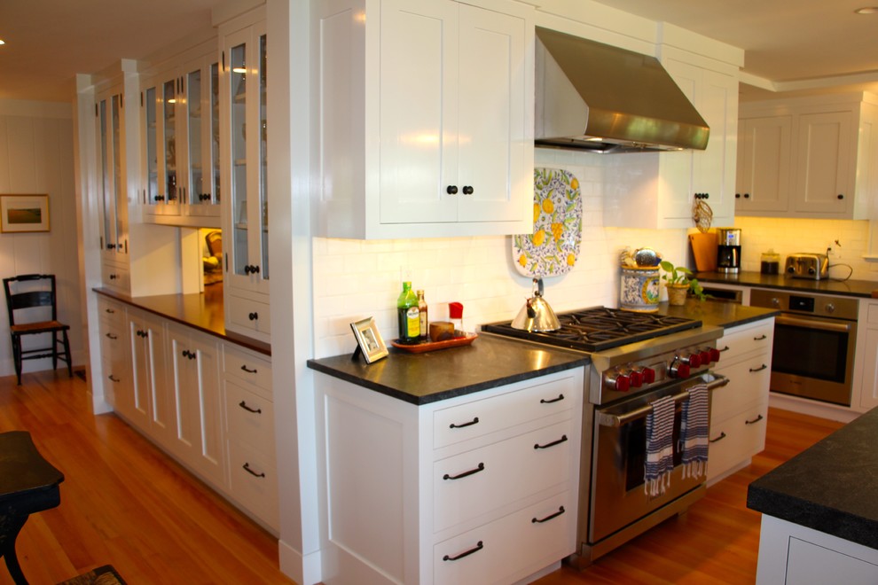 Bild på ett stort lantligt kök, med en undermonterad diskho, skåp i shakerstil, vita skåp, bänkskiva i täljsten, vitt stänkskydd, stänkskydd i tunnelbanekakel, rostfria vitvaror, mellanmörkt trägolv, en köksö och brunt golv