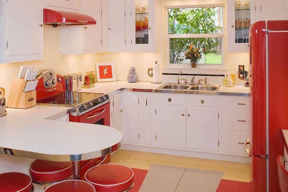 Inspiration for a small midcentury l-shaped kitchen in Tampa with a double-bowl sink, flat-panel cabinets, white cabinets, white splashback, ceramic splashback, coloured appliances and lino flooring.