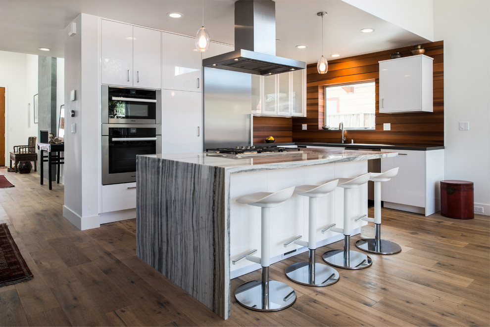 Small trendy l-shaped dark wood floor and brown floor open concept kitchen photo in San Francisco with a drop-in sink, flat-panel cabinets, white cabinets, marble countertops, brown backsplash, wood backsplash, stainless steel appliances, an island and gray countertops