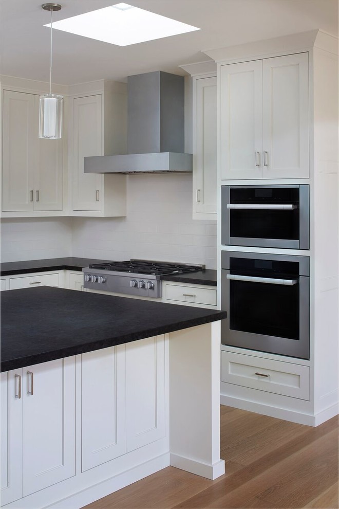 Inspiration för moderna kök, med luckor med infälld panel, vita skåp, vitt stänkskydd, stänkskydd i porslinskakel, mellanmörkt trägolv, en köksö, en undermonterad diskho, granitbänkskiva och integrerade vitvaror