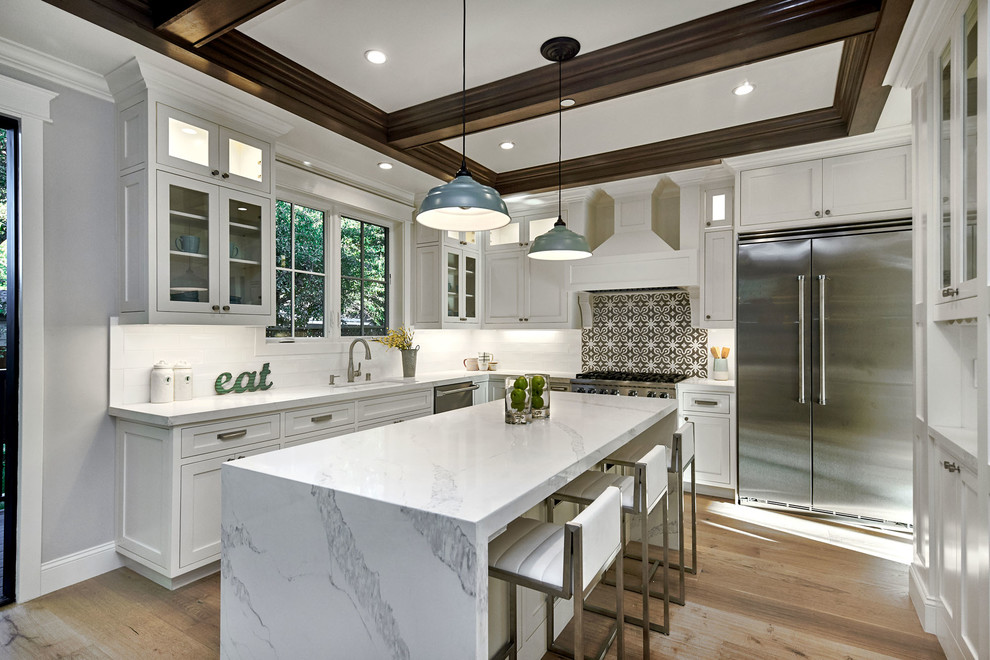 Example of a mid-sized transitional u-shaped light wood floor and beige floor kitchen design in San Francisco with an undermount sink, shaker cabinets, white cabinets, quartz countertops, white backsplash, cement tile backsplash, stainless steel appliances, an island and white countertops