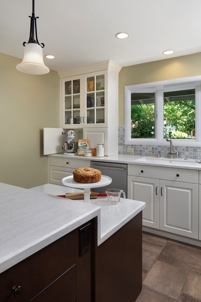Exempel på ett klassiskt vit vitt kök, med en undermonterad diskho, luckor med upphöjd panel, bänkskiva i kvarts, flerfärgad stänkskydd, stänkskydd i mosaik, rostfria vitvaror, klinkergolv i porslin, en köksö och brunt golv