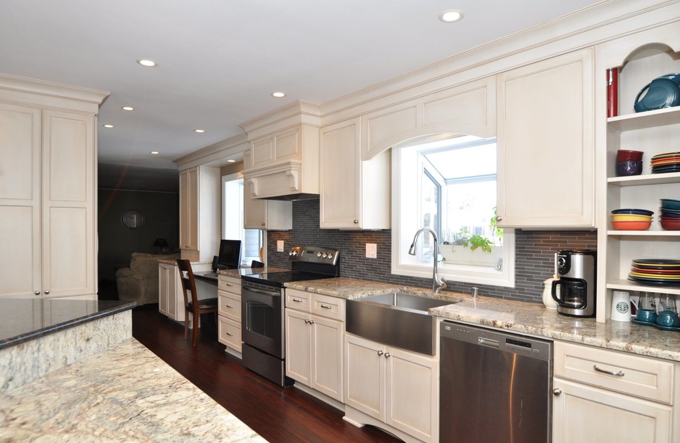 Example of a mid-sized classic medium tone wood floor eat-in kitchen design in Milwaukee with stainless steel appliances, a farmhouse sink, raised-panel cabinets, white cabinets, granite countertops, gray backsplash, glass tile backsplash and an island