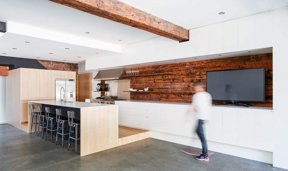 Modern inredning av ett kök, med en undermonterad diskho, släta luckor, rostfria vitvaror, betonggolv, en köksö och stänkskydd med metallisk yta