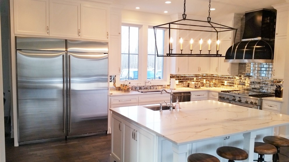 Exempel på ett stort klassiskt kök, med en undermonterad diskho, luckor med infälld panel, vita skåp, marmorbänkskiva, stänkskydd med metallisk yta, spegel som stänkskydd, rostfria vitvaror, mörkt trägolv och en köksö