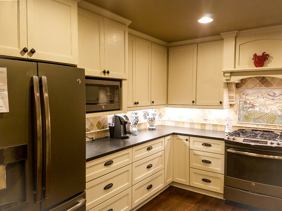 Klassisk inredning av ett stort kök, med en undermonterad diskho, luckor med infälld panel, vita skåp, granitbänkskiva, beige stänkskydd, stänkskydd i travertin, rostfria vitvaror, mörkt trägolv, en halv köksö och brunt golv