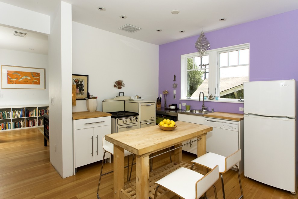 Cette photo montre une cuisine tendance en L avec un placard à porte plane, des portes de placard blanches, un plan de travail en bois et un électroménager blanc.