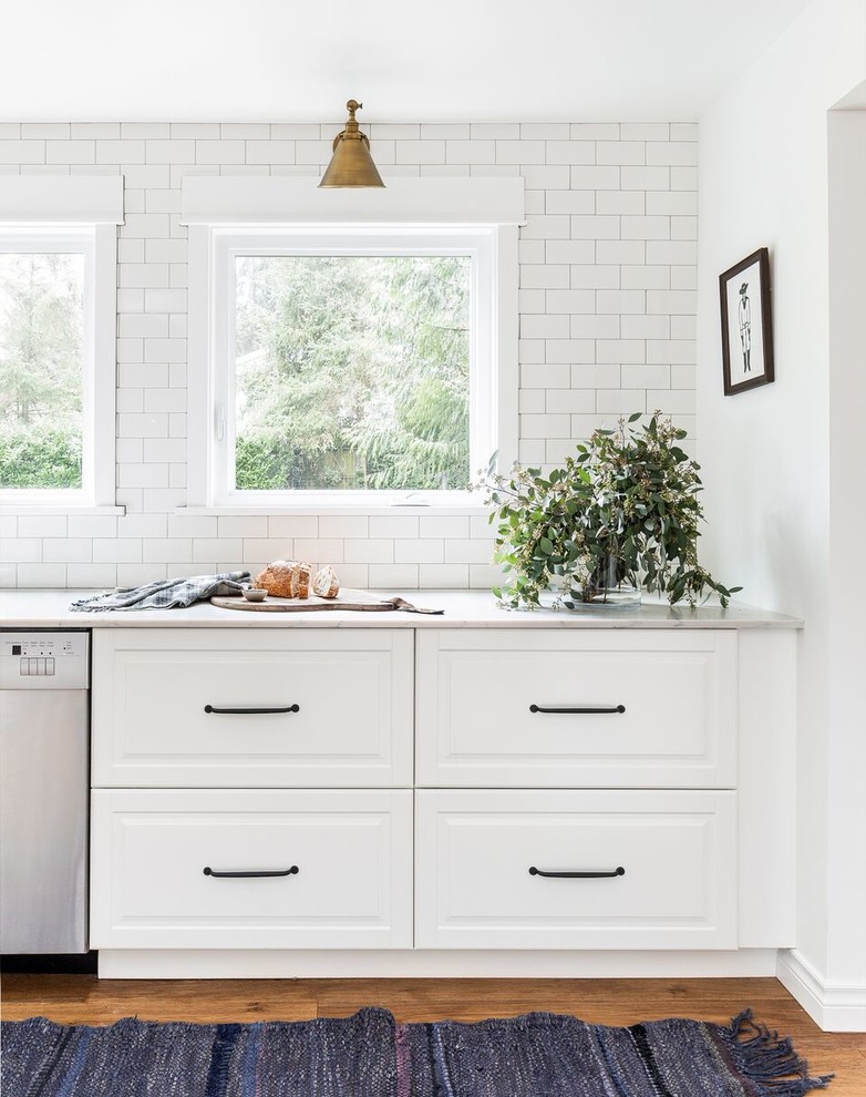 Landhaus Küche mit profilierten Schrankfronten, weißen Schränken, Küchenrückwand in Weiß, Rückwand aus Metrofliesen, Küchengeräten aus Edelstahl, braunem Holzboden und braunem Boden in Seattle
