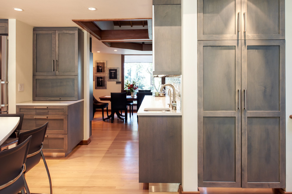 Exempel på ett mellanstort modernt kök, med en nedsänkt diskho, skåp i shakerstil, grå skåp, bänkskiva i kvarts, blått stänkskydd, stänkskydd i glaskakel, rostfria vitvaror, ljust trägolv och en köksö