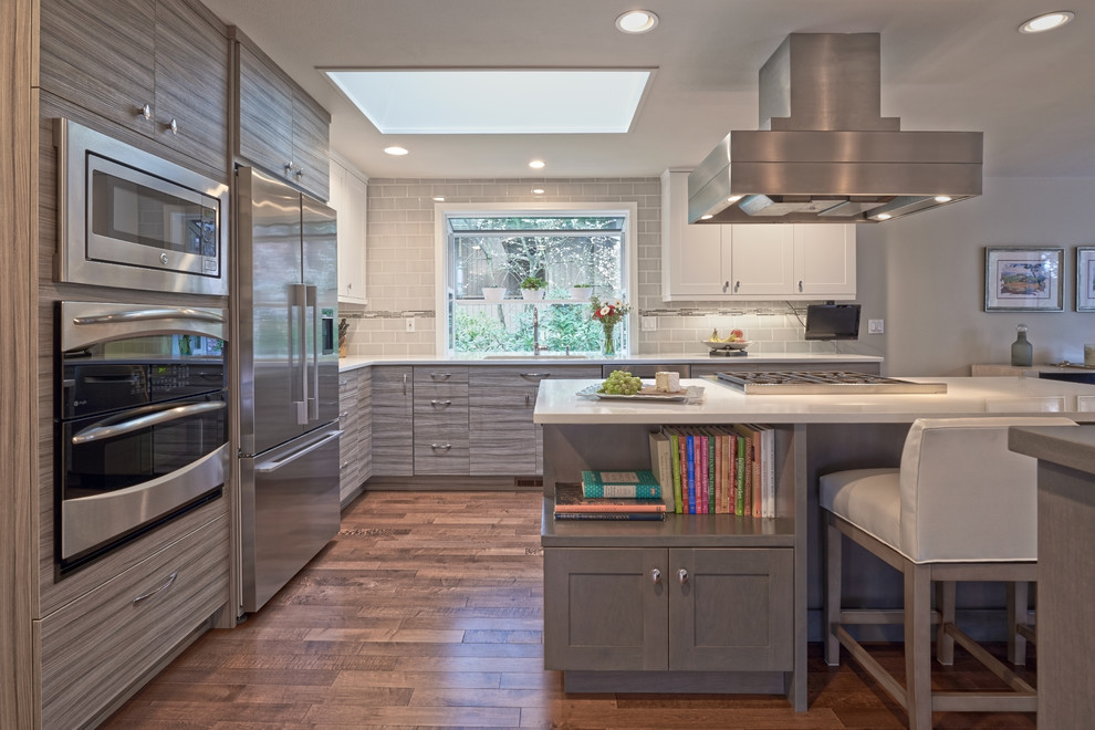 Photo of a contemporary l-shaped kitchen in Seattle with a submerged sink, flat-panel cabinets, grey cabinets, engineered stone countertops, grey splashback, metro tiled splashback, stainless steel appliances, dark hardwood flooring and multiple islands.