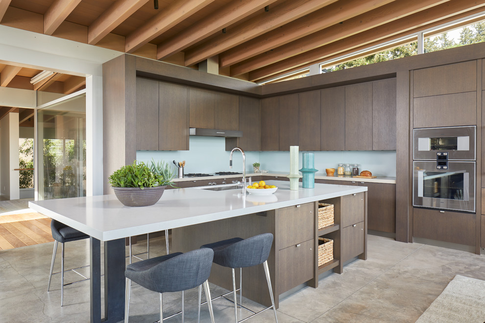 Inspiration for a large modern l-shaped open plan kitchen in Seattle with a submerged sink, flat-panel cabinets, medium wood cabinets, engineered stone countertops, blue splashback, glass sheet splashback, stainless steel appliances, concrete flooring, an island, grey floors and grey worktops.
