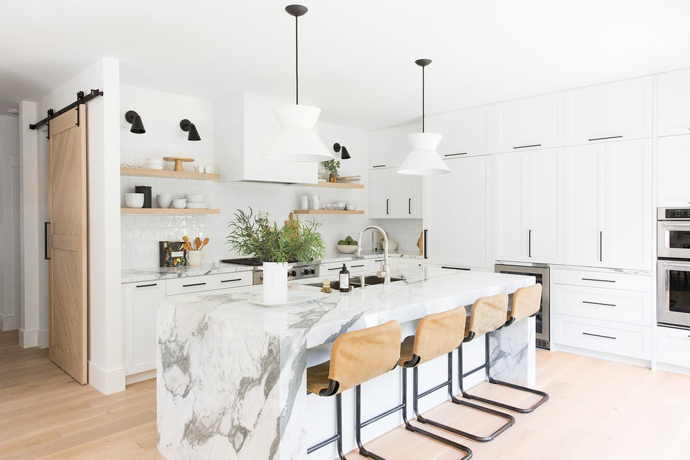 Photo of a traditional l-shaped kitchen/diner in Salt Lake City with white cabinets, marble worktops, white splashback, integrated appliances, light hardwood flooring, an island, a double-bowl sink, shaker cabinets, beige floors and white worktops.