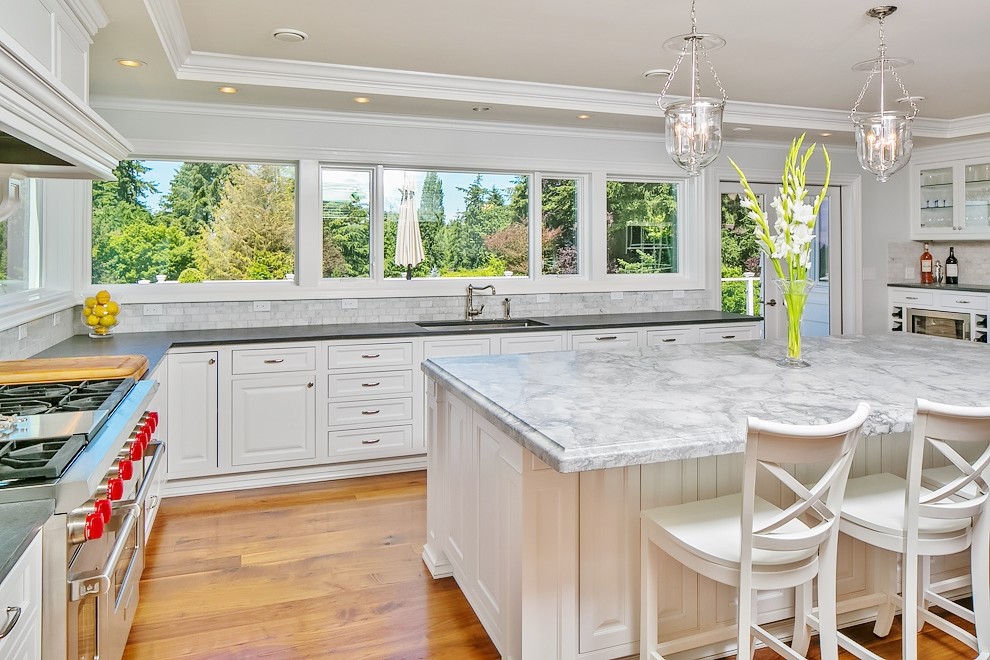 Eat-in kitchen - huge transitional u-shaped medium tone wood floor eat-in kitchen idea in Seattle with an undermount sink, raised-panel cabinets, white cabinets, soapstone countertops, gray backsplash, ceramic backsplash, stainless steel appliances and an island