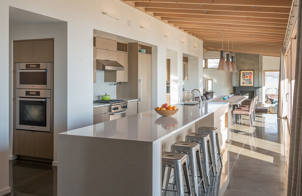 Medium sized contemporary single-wall kitchen/diner in Seattle with a single-bowl sink, flat-panel cabinets, light wood cabinets, white splashback, stainless steel appliances, concrete flooring, an island and grey floors.