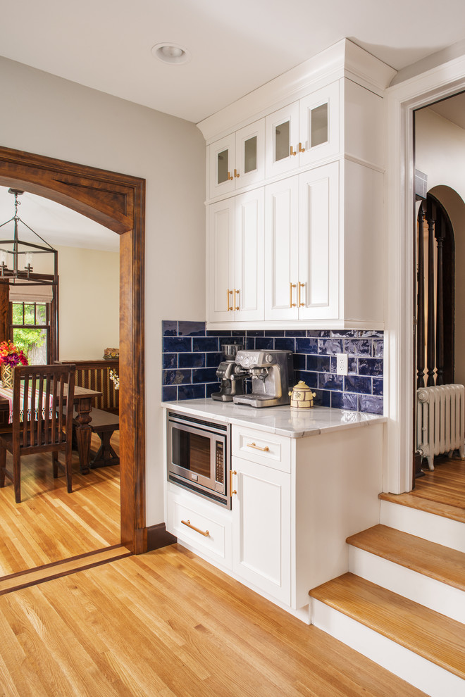 Bild på ett vintage vit vitt kök, med vita skåp, bänkskiva i kvarts, blått stänkskydd, stänkskydd i porslinskakel, rostfria vitvaror och ljust trägolv