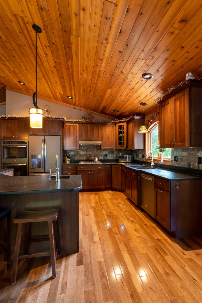 Inspiration for a mid-sized rustic l-shaped medium tone wood floor, brown floor and wood ceiling open concept kitchen remodel in Burlington with an undermount sink, recessed-panel cabinets, medium tone wood cabinets, gray backsplash, stainless steel appliances, an island and black countertops