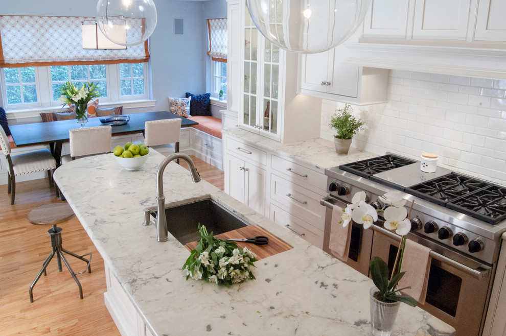 Example of a mid-sized transitional l-shaped medium tone wood floor eat-in kitchen design in Philadelphia with an undermount sink, shaker cabinets, white cabinets, quartzite countertops, white backsplash, ceramic backsplash, stainless steel appliances and an island