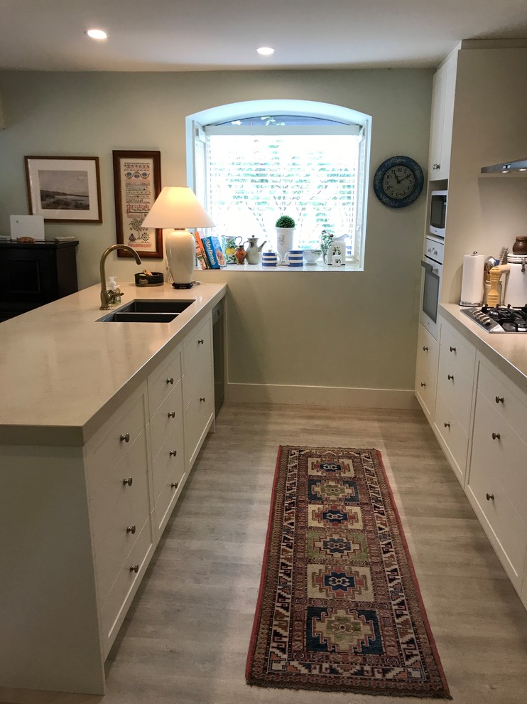 Inspiration for a mid-sized timeless galley light wood floor and multicolored floor open concept kitchen remodel in Christchurch with a double-bowl sink, shaker cabinets, white cabinets, quartz countertops, blue backsplash, glass tile backsplash, white appliances and a peninsula
