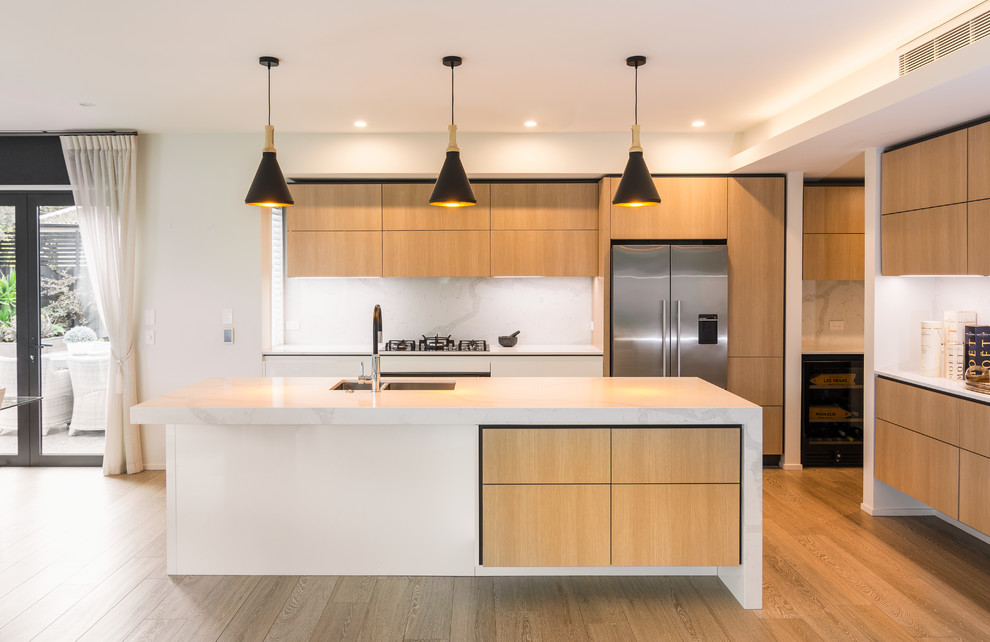 Modern inredning av ett stort kök och matrum, med en undermonterad diskho, skåp i ljust trä, bänkskiva i kvarts, vitt stänkskydd, stänkskydd i marmor, rostfria vitvaror, ljust trägolv, en köksö och brunt golv