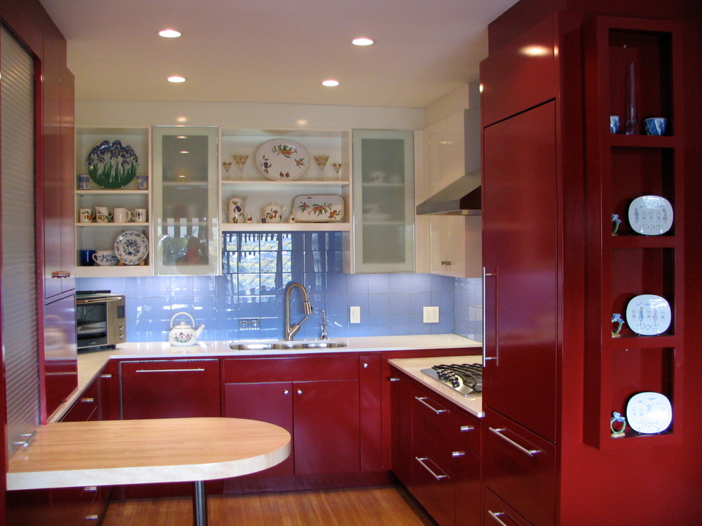 Inredning av ett modernt mellanstort u-kök, med en undermonterad diskho, släta luckor, röda skåp, bänkskiva i kvarts, blått stänkskydd, stänkskydd i porslinskakel, integrerade vitvaror, mellanmörkt trägolv, en halv köksö och brunt golv