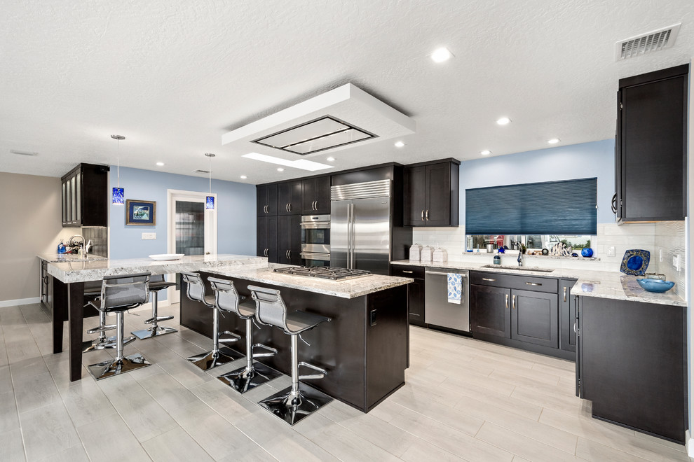 Inspiration for a large contemporary l-shaped open plan kitchen in Orlando with a built-in sink, recessed-panel cabinets, grey cabinets, granite worktops, white splashback, metro tiled splashback, stainless steel appliances, light hardwood flooring, an island and grey floors.