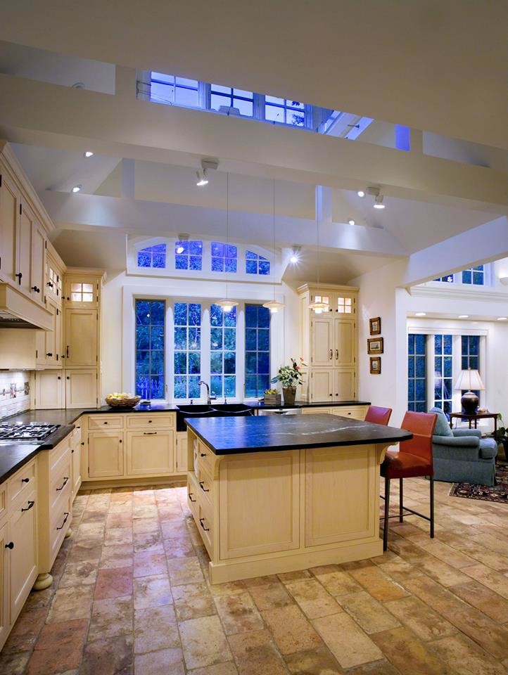 Mid-sized elegant l-shaped terra-cotta tile and multicolored floor enclosed kitchen photo in Newark with a farmhouse sink, beaded inset cabinets, beige cabinets, soapstone countertops, beige backsplash, stone tile backsplash, stainless steel appliances and an island