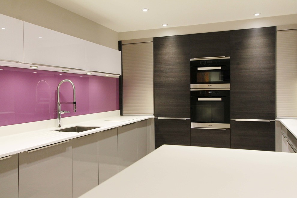 Medium sized contemporary u-shaped kitchen/diner in London with a built-in sink, flat-panel cabinets, dark wood cabinets, composite countertops, pink splashback, glass sheet splashback, stainless steel appliances and a breakfast bar.
