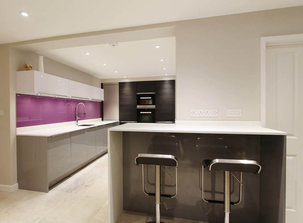 Example of a mid-sized trendy u-shaped eat-in kitchen design in London with a drop-in sink, flat-panel cabinets, dark wood cabinets, solid surface countertops, pink backsplash, glass sheet backsplash, stainless steel appliances and a peninsula