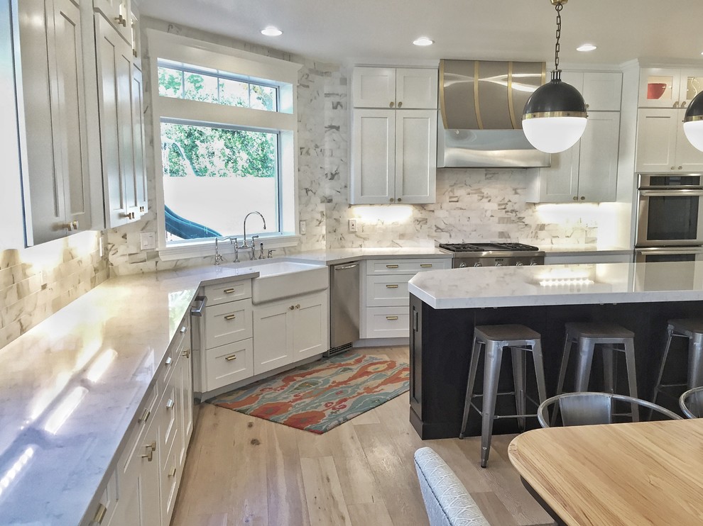 Large transitional l-shaped laminate floor and beige floor eat-in kitchen photo in Phoenix with a farmhouse sink, shaker cabinets, white cabinets, quartz countertops, white backsplash, marble backsplash, stainless steel appliances, an island and white countertops
