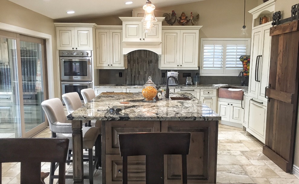 Bild på ett stort vintage flerfärgad flerfärgat kök, med en rustik diskho, luckor med upphöjd panel, vita skåp, granitbänkskiva, grått stänkskydd, stänkskydd i glaskakel, rostfria vitvaror, travertin golv, en köksö och beiget golv